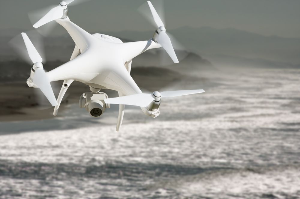Unmanned Aircraft System (UAV) Quadcopter Drone In The Air Over The Ocean Coastline.