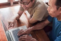 Happy adult son teaching older father using laptop