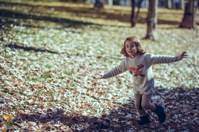 Happy child running in park of colorful fall leaves with her arms open