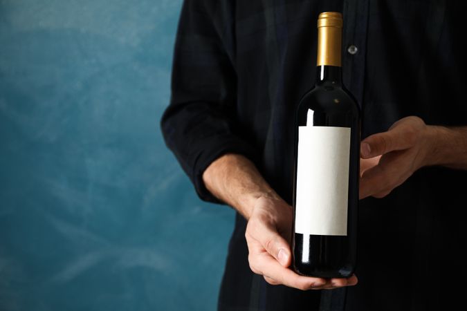 Man in shirt hold bottle of wine with empty space against blue background