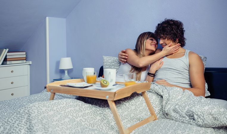 Couple smiling and hugging while eating breakfast in bed