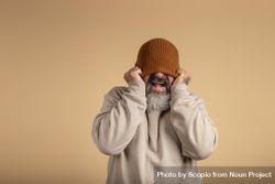 Studio portrait of an over excited man hiding his eyes with brown knit cap 4mBZ7b