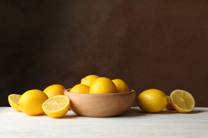 Wooden bowl and lemons against brown background, space for text