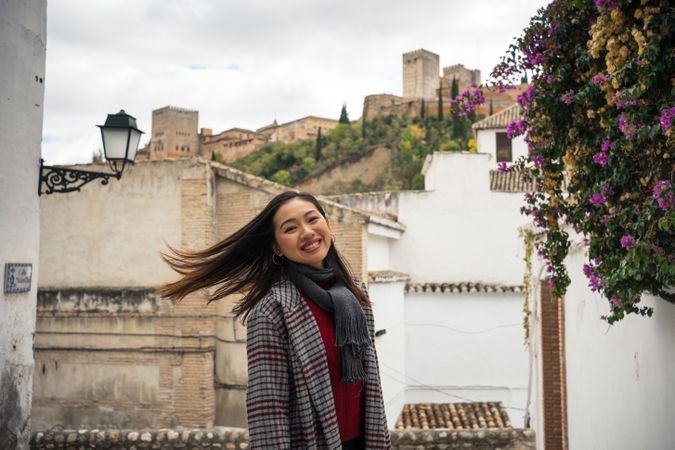 Asian female traveler in warm wear smiling among old buildings near big castle