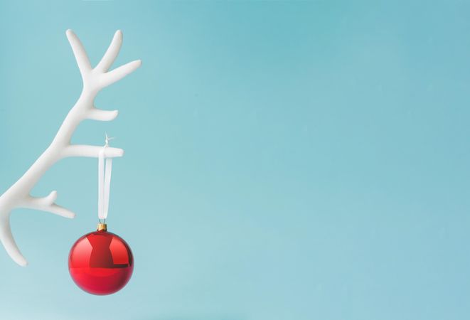 Reindeer antler with red Christmas bauble decoration on pastel blue background