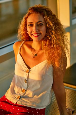 Stylish cheerful woman sitting on metal bench in glass hallway of airport in Texas