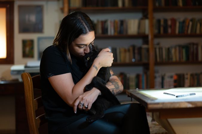 Woman sitting at her desk in a studio holding a dark colored cat