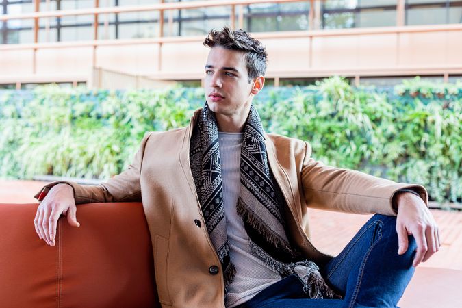 Young man wearing winter clothes sitting on a leather bench outside