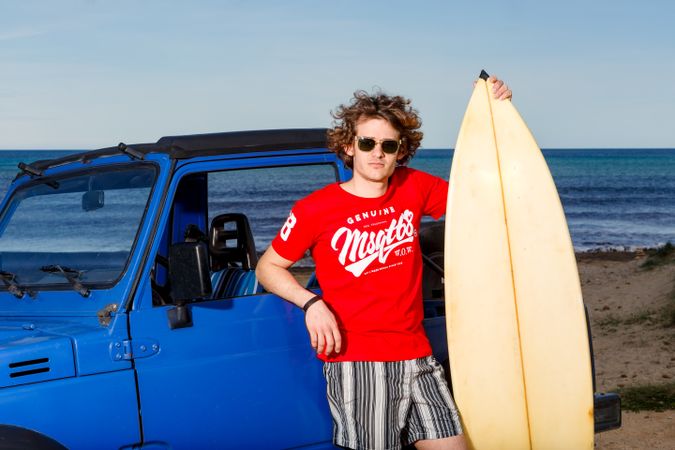 Guy with big surfboard near car on beach