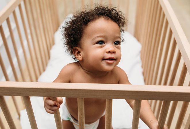 Cute baby boy standing up looking over his crib