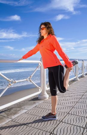 Athletic woman stretching legs before running on the beach promenade on a summer morning