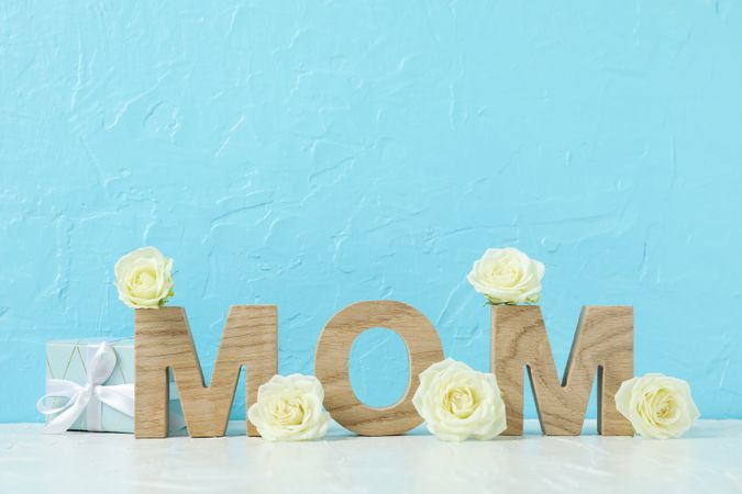 Inscription Mom with roses on pink table against color background, space for text