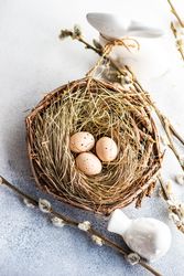 Top view of speckled eggs in nest on table with pussy willow branches and rabbit figurines with copy space