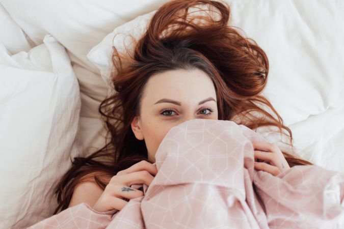 Woman in bed hiding her face under pink blanket