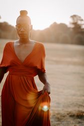 Woman in orange v neck dress standing in grass field