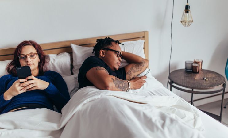 Man and woman busy with their cell phones in bed