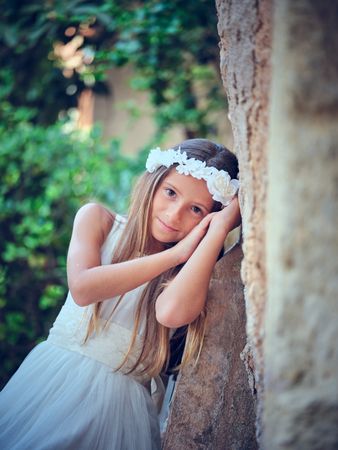 Young woman in bridal dress leaning on wall while looking at cam