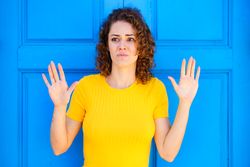 Defensive woman in yellow dress against a closed blue door