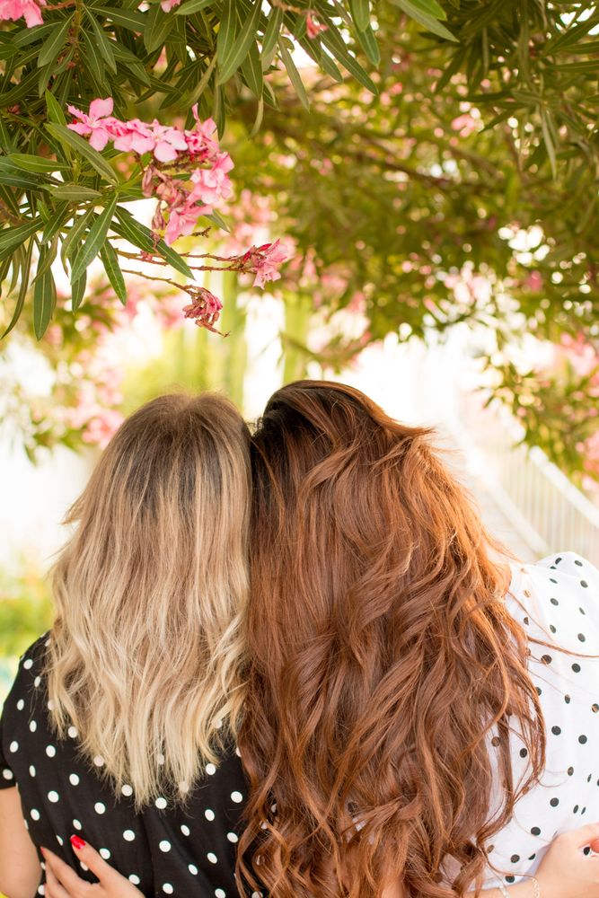 Back view of two women leaning on each other under a tree
