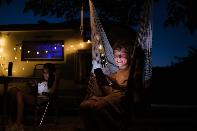 Delighted boy using smartphone in hammock outside trailer