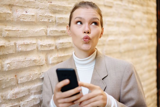 A Young Woman Joyfully and Playfully Posing with Her Phone Against a Textured Wall