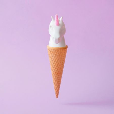 Painted unicorn head in ice cream cone on pastel purple background