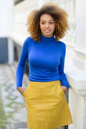 Female with curly hair and boots wearing bright clothes pictured outside