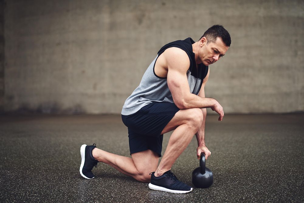 Man in vest kneeling down on one knee with kettlebell