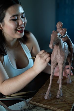 Cool young woman in white tank sculpting with clay