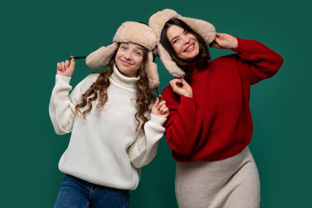 Mum and teenage daughter wear matching furry winter hats, grinning