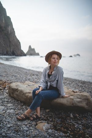 Woman resting on beach stone by sea