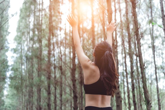 Woman stretching arms up to sun in forest