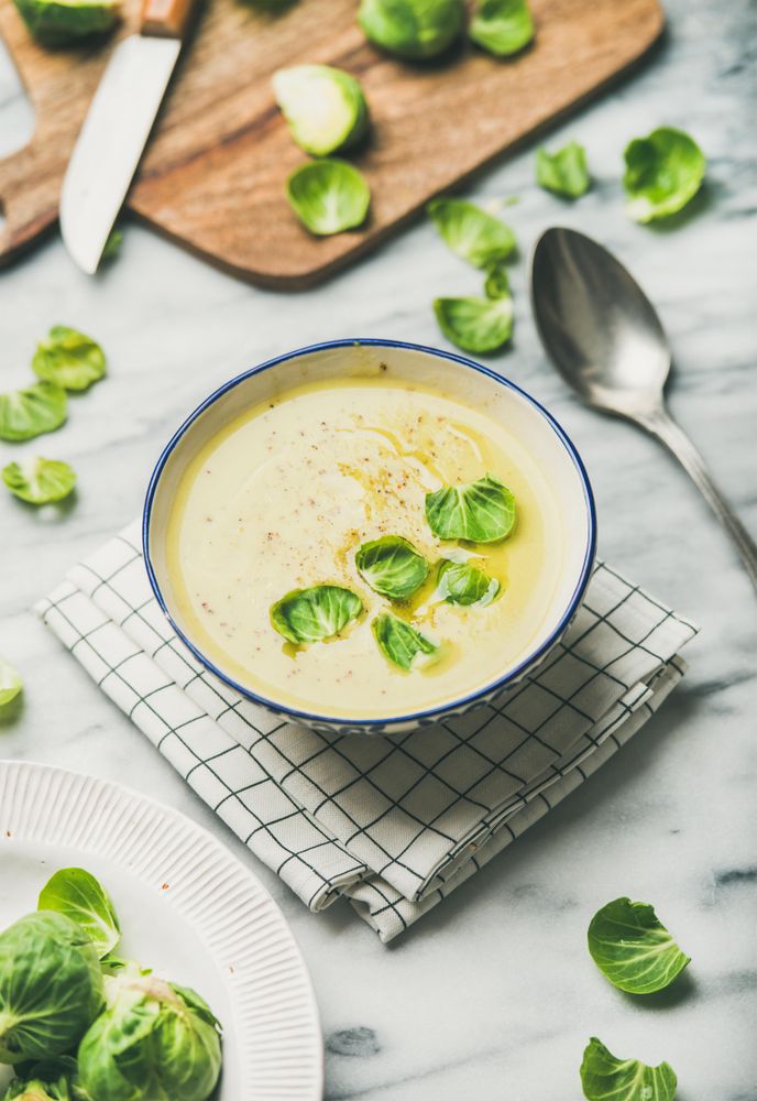 Brussels sprout soup, garnished with fresh sprouts, next to wooden board, vertical composition