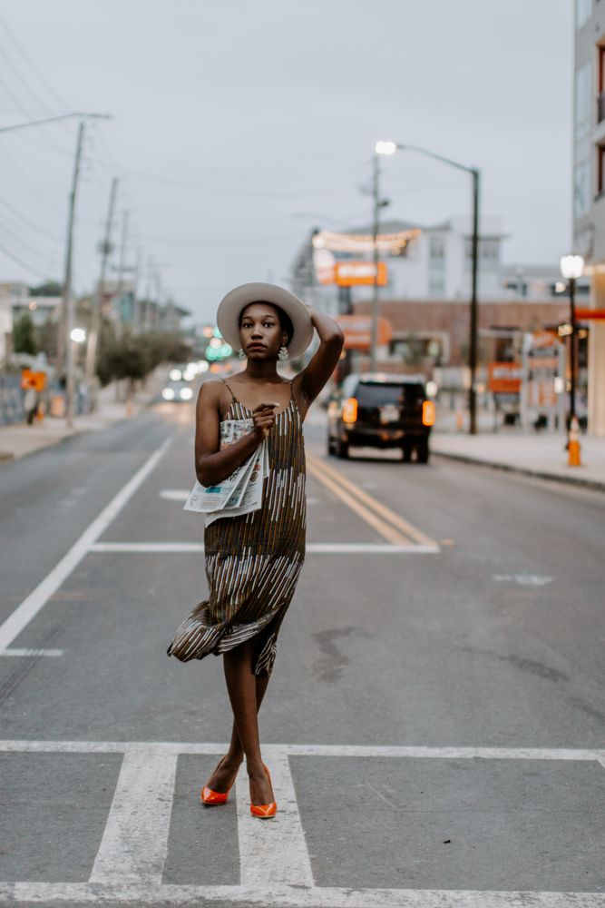 Woman standing in the middle of the road wearing red heels holding a newspaper