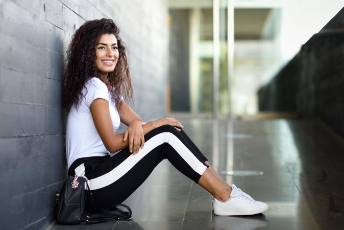 Happy female in leggings sitting outside of building entrance