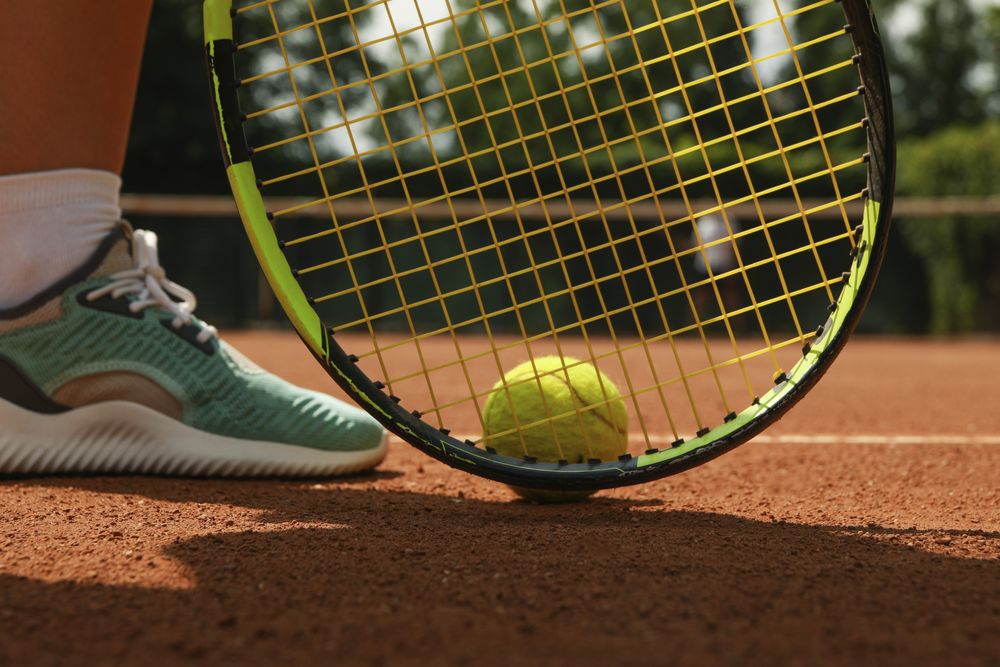 Woman leg, racket and tennis ball on clay court