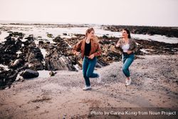Two trendy young women running playfully along the beach n56gl4