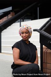 Portrait of confident Black nurse in head covering sitting on steps in front of medical building 432Yj5