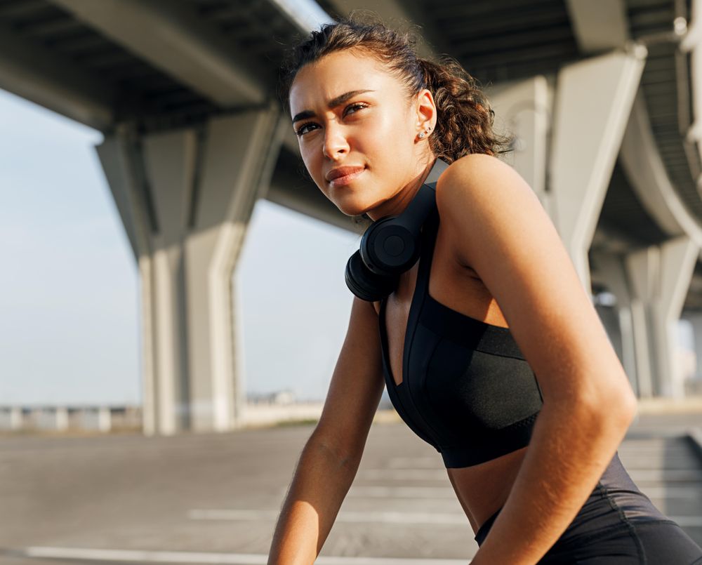Woman under a bridge in athletic gear and headphones