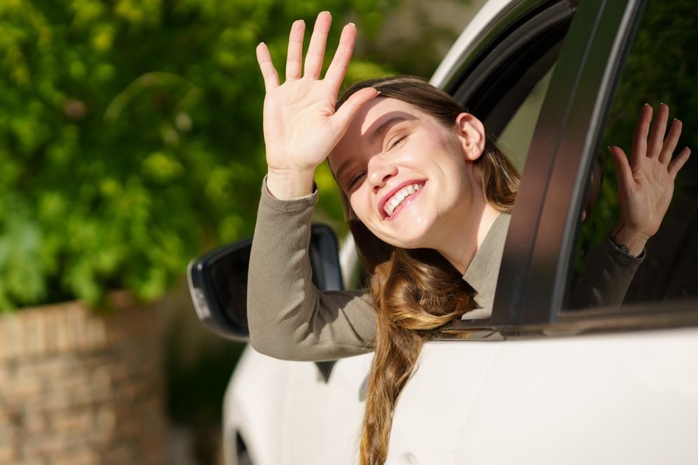 A Joyful Girl Cheerfully Waving from the Open Window of a Car Surrounded by Beautiful Nature