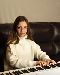 Girl in white sweater playing piano, looking at camera.