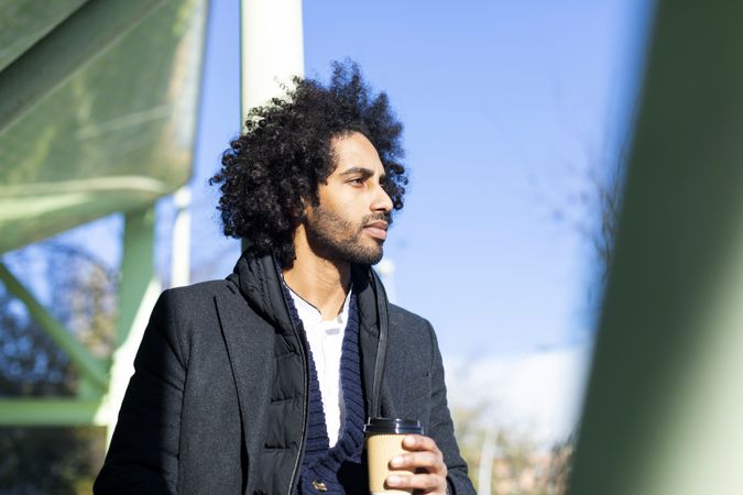 Black man in jacket holding warm beverage while looking in the distance