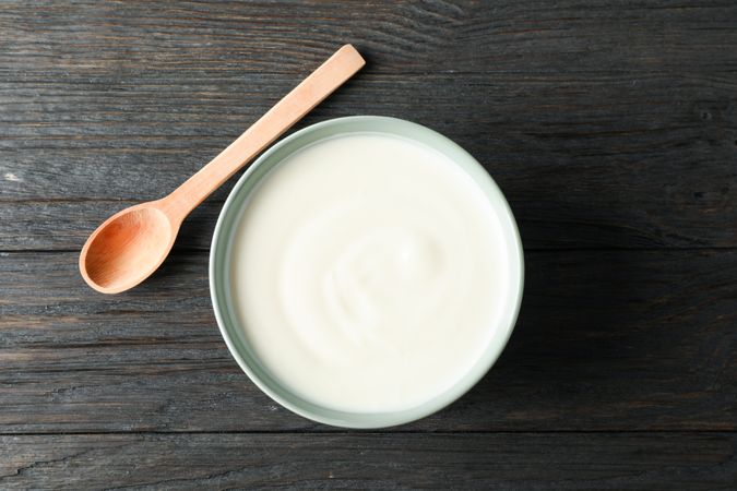 Bowl of sour cream yogurt and spoon on wooden background