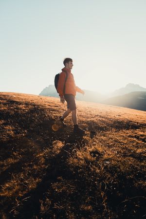 Side view of young man with backpack hiking in Dolomites, Italy at sunset