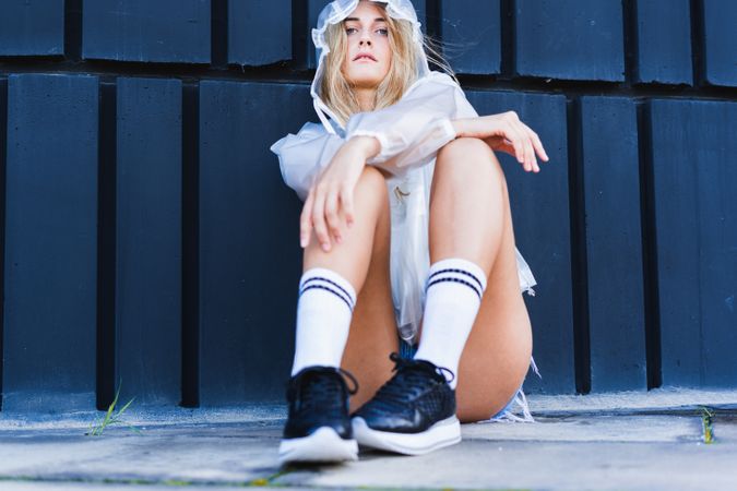 Charming stylish woman in raincoat sitting near wall