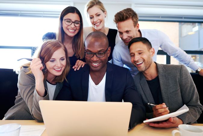 Happy business associates huddled around a laptop in an office