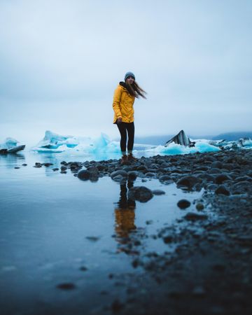 Young woman in yellow jacket standing on snow covered rocky shore in Bothell, Washington, United States