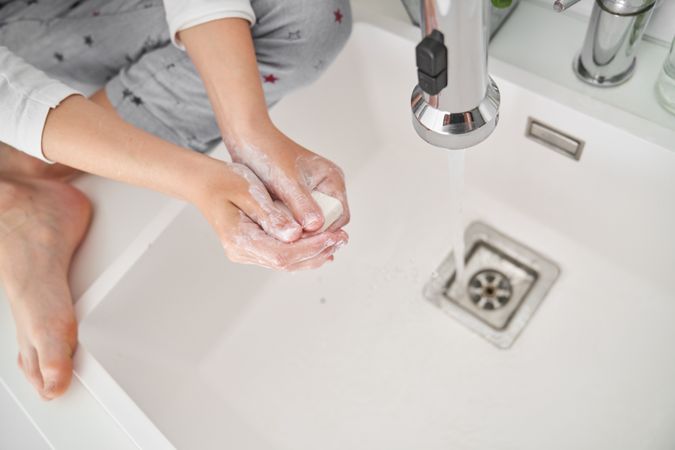 Kid washing hands with soap in sink in bathroom