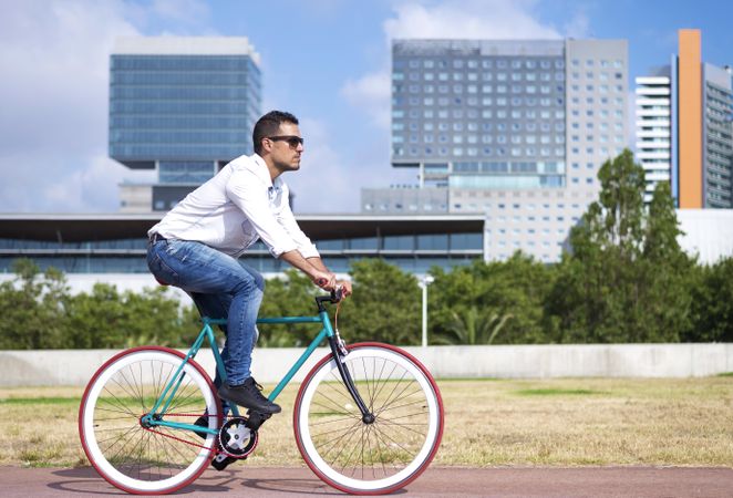 Male riding red and green bike outside next to city buildings on nice day