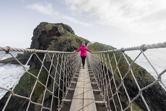 Woman crossing rope bridge leading to rocky island